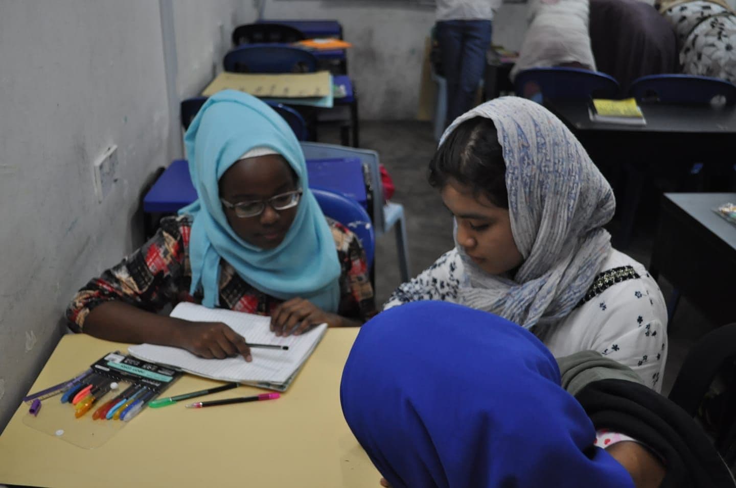 Students working with coloured pencils at a shared table in class.